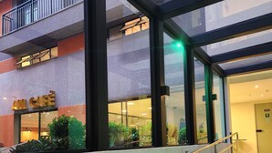 Un bâtiment moderne avec un café au rez-de-chaussée, des rampes en verre et un escalier illuminé de lumière verte.