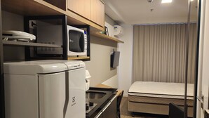 Une chambre d’hôtel de taille réduite, dotée d’une kitchenette, d’un lit et d’une fenêtre avec des rideaux.