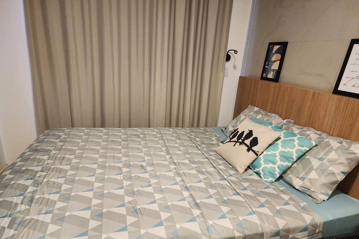 A neatly made bed with a geometric patterned bedspread, two pillows with a bird design, and a wooden headboard.