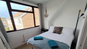 Ein Schlafzimmer mit Bett, Fenster, Heizkörper und einer wandmontierten Lampe.