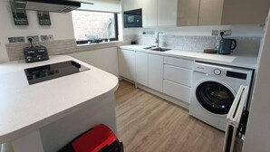 Eine moderne Küche mit weißen Schränken, einem eingebauten Backofen, einer Waschmaschine und einem Fenster, das für natürliches Licht sorgt.