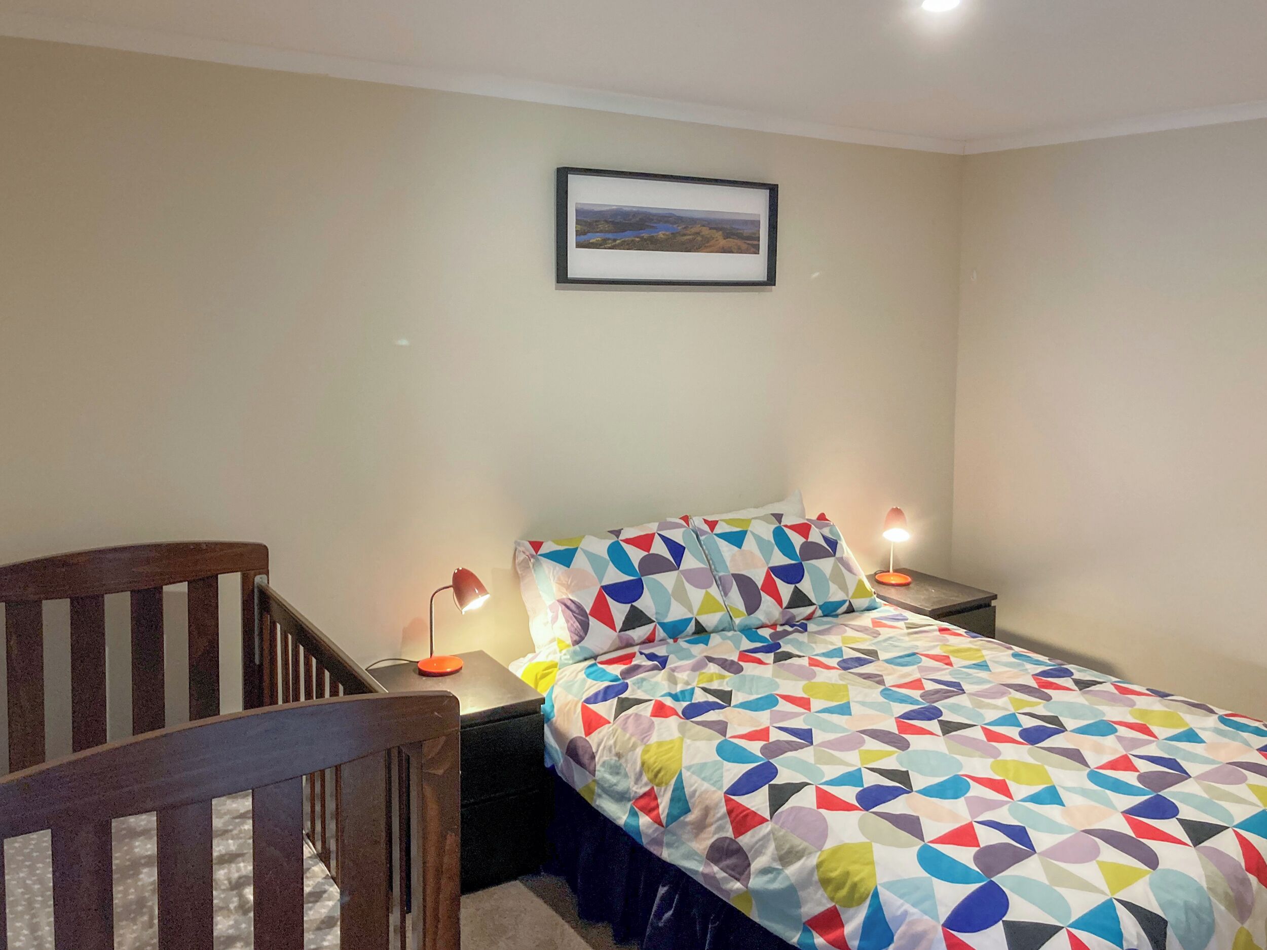 A bedroom with a bed, a nightstand, a desk, a chair, and a framed picture on the wall.