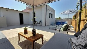 Relax on the spacious patio, featuring a comfortable sofa, a wooden table, and a metal chair, all shaded under a large canopy.