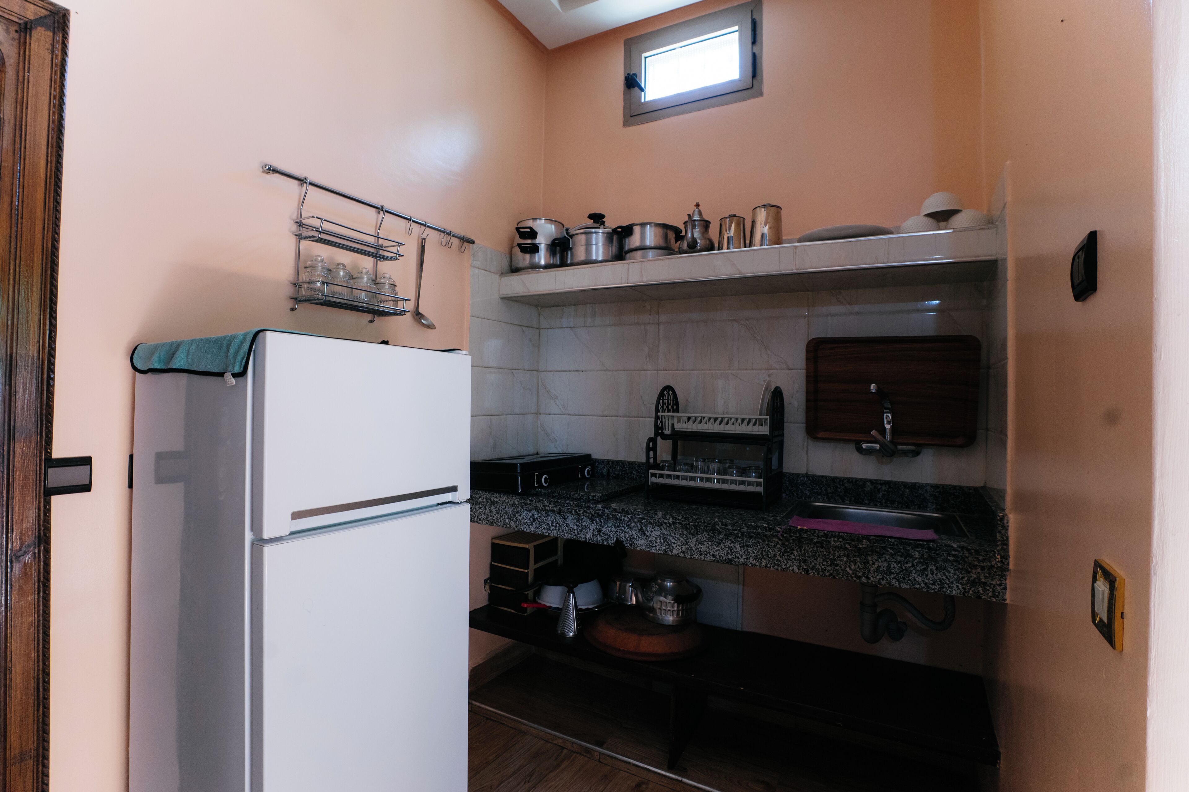 Eine kleine Küche mit Kühlschrank, Spüle, einer Arbeitsplatte mit verschiedenen Küchenutensilien und einem Fenster über der Spüle.
