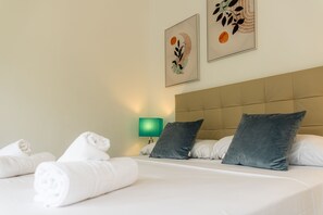 Uma cama bem arrumada com lençóis brancos e duas almofadas, uma luminária verde na parede e duas obras de arte emolduradas acima da cama.