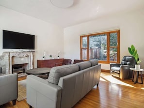 A modern living room with a fireplace, leather sofa, and a large window with a view of a backyard.