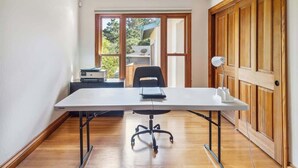 Une pièce comprenant une grande table, une chaise, un bureau avec un ordinateur et une porte donnant sur l’extérieur.