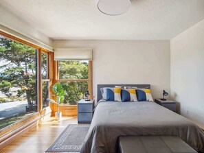 Une chambre à coucher moderne avec un grand lit, des tables de chevet, une commode et une fenêtre donnant sur des arbres.