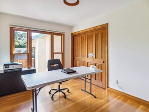 A room with a wooden floor, a white desk with a chair, a printer, and a door with a wooden panel.