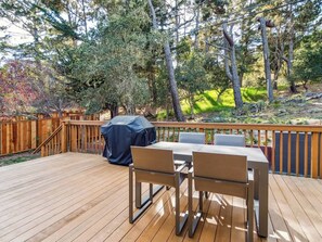 Une terrasse en bois avec une table et des chaises, entourée d’une clôture en bois et d’arbres.