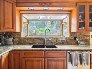 A kitchen with wooden cabinets, granite countertops, a double sink, and a window with a view of trees.