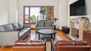 Un salon comprenant un canapé, un fauteuil, une table basse, un pouf en cuir, une cheminée et un téléviseur.