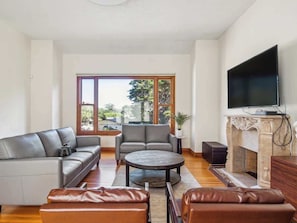 A living room with a sofa, armchair, coffee table, leather ottoman, fireplace, and a TV.