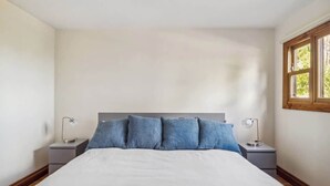 Une chambre avec un grand lit, deux tables de chevet et une fenêtre donnant sur un paysage verdoyant.