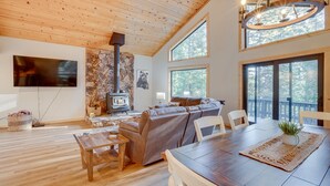 Un vaste salon doté d’un plafond en bois, d’une cheminée, d’un grand canapé et d’un coin repas avec une table et des chaises.