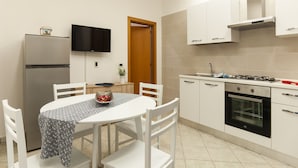 Una cocina compacta con armarios blancos, horno empotrado, cocina a gas y televisor de pantalla plana montado en la pared.