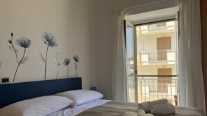 Una cama bien hecha con sábanas blancas y toallas enrolladas, un cabecero azul y una pared decorada con motivos florales.