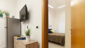 Una cocina moderna con refrigerador, un mueble de madera, una planta en maceta y un televisor de pantalla plana montado en la pared.