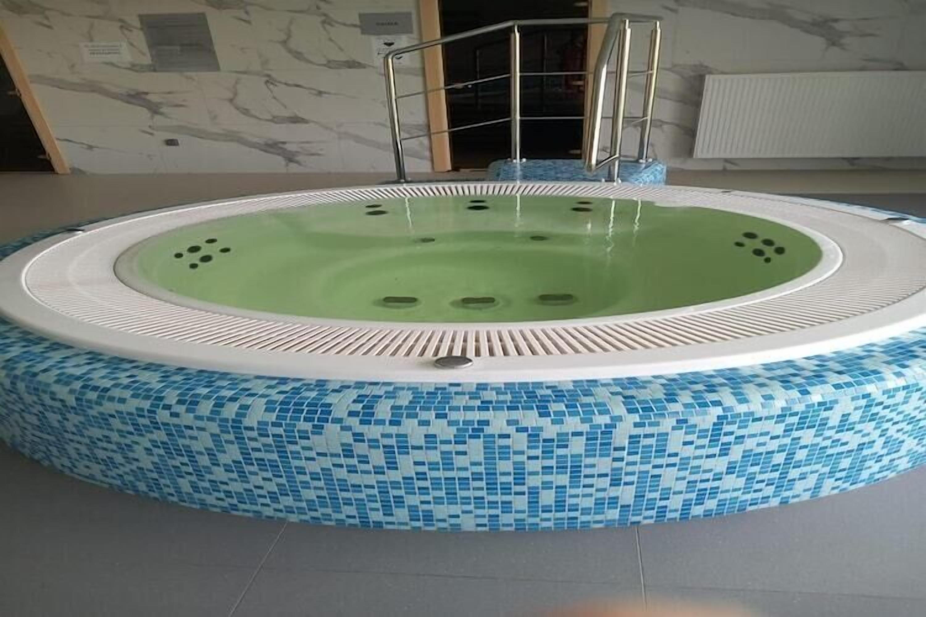 Un jacuzzi rond, avec un intérieur vert et un extérieur orné d’une mosaïque bleue.