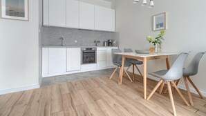 A modern kitchen with white cabinets, a grey countertop, and a wooden floor. There is a dining table with grey chairs and a vase with flowers. - Comfortable apartment, indoor pool and sauna (Dziwnow)