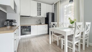 A modern kitchen with white cabinets, a built-in oven, and a dining area with a white table and chairs. - Comfortable apartment by the sea (Pobierowo)