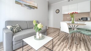 A modern living room with a grey sofa, a white coffee table with a vase of flowers, and a dining area with a round table and chairs.