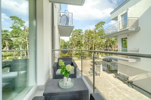 Un balcon agrémenté de meubles en osier, une table en verre avec des bougies et une vue sur un quartier résidentiel, avec ses arbres et ses voitures garées.