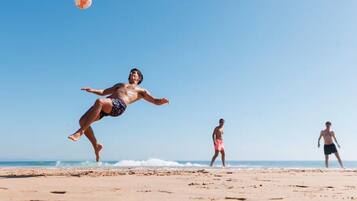 En strandscen med en person som hoppar och en volleyboll i luften.