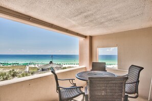 Un balcon agrémenté de meubles en osier, une vue sur la plage et un ciel dégagé.