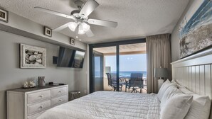 Une chambre dotée d’un grand lit, d’un ventilateur de plafond, d’une commode, d’un téléviseur et offrant une vue sur l’océan grâce à une porte-fenêtre coulissante.