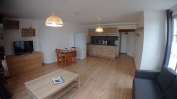 A spacious living room with a wooden floor, a dining area with a table and chairs, a kitchen with modern appliances, and a large window providing natural light.
