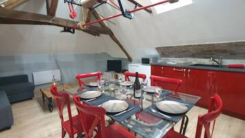 A dining area with a high ceiling, exposed wooden beams, and red chairs. A table is set with plates, glasses, and a bottle.