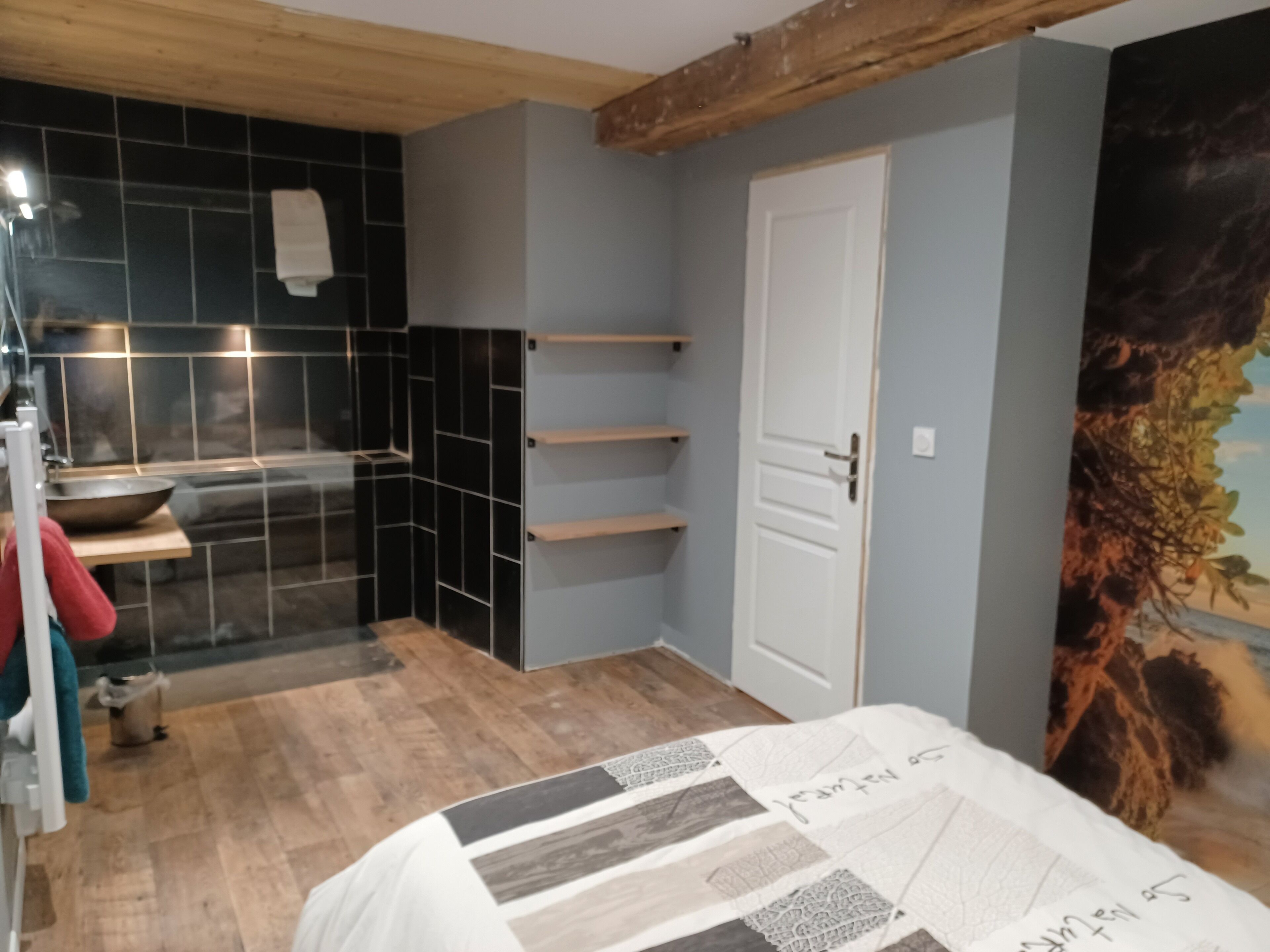 Et moderne badeværelse med bruser, vask og toilet. Et håndklæde hænger på væggen, og der er en hylde med toiletartikler.