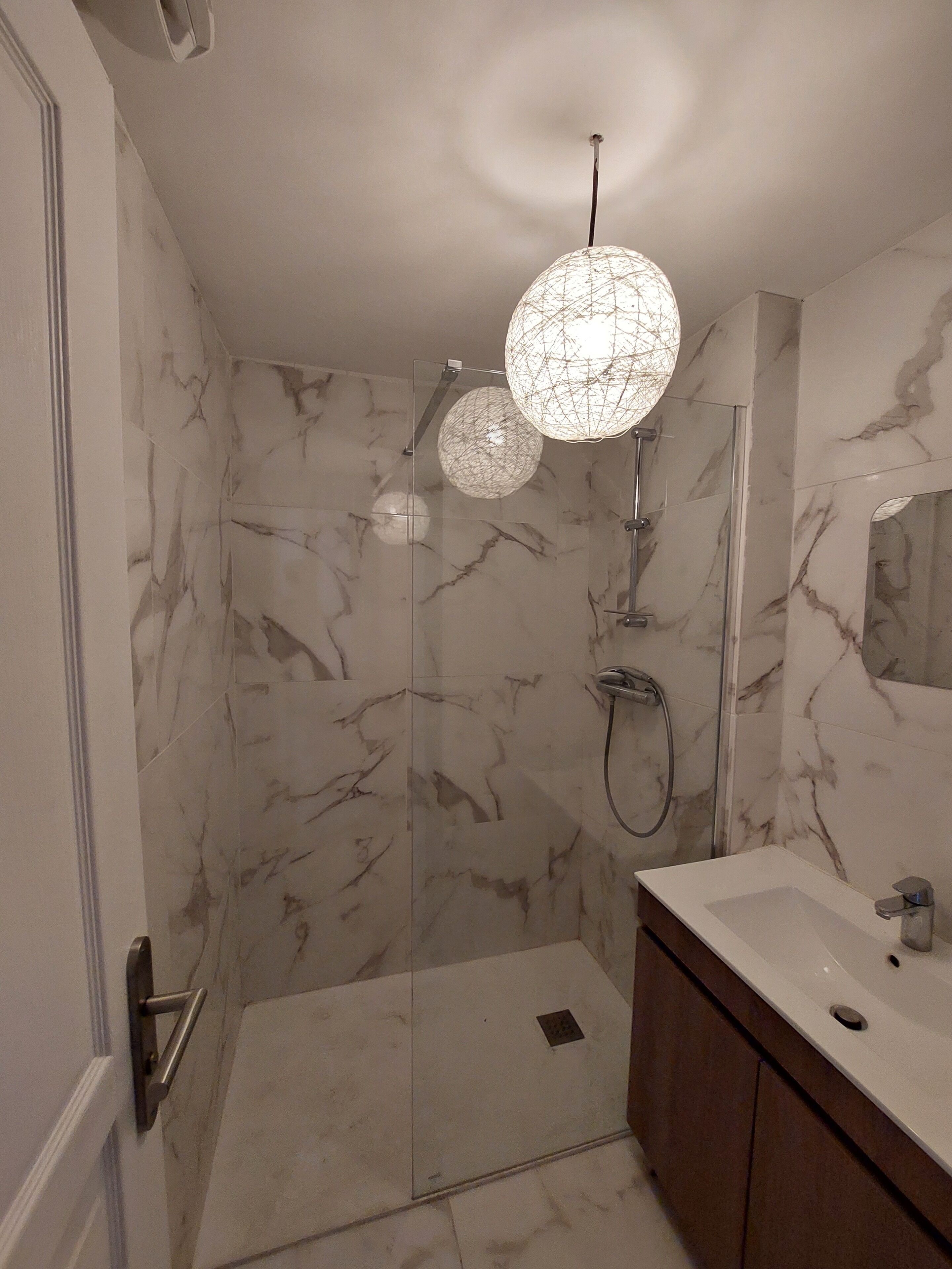 A modern bathroom with a glass-enclosed shower, marble walls, and a vanity with a mirror.