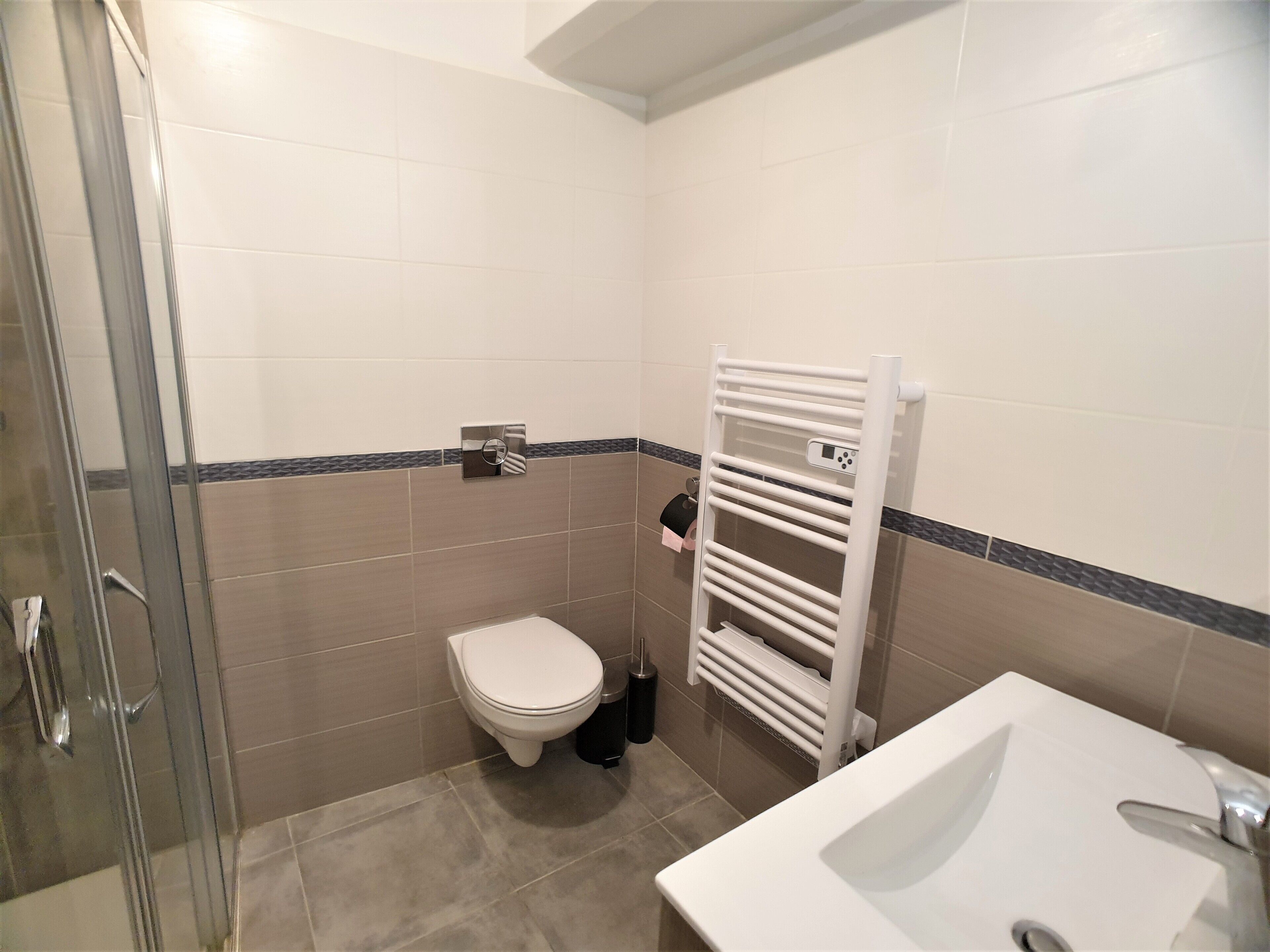 Ein Badezimmer mit Toilette, Waschbecken, Duschkabine aus Glas und Handtuchhalter.