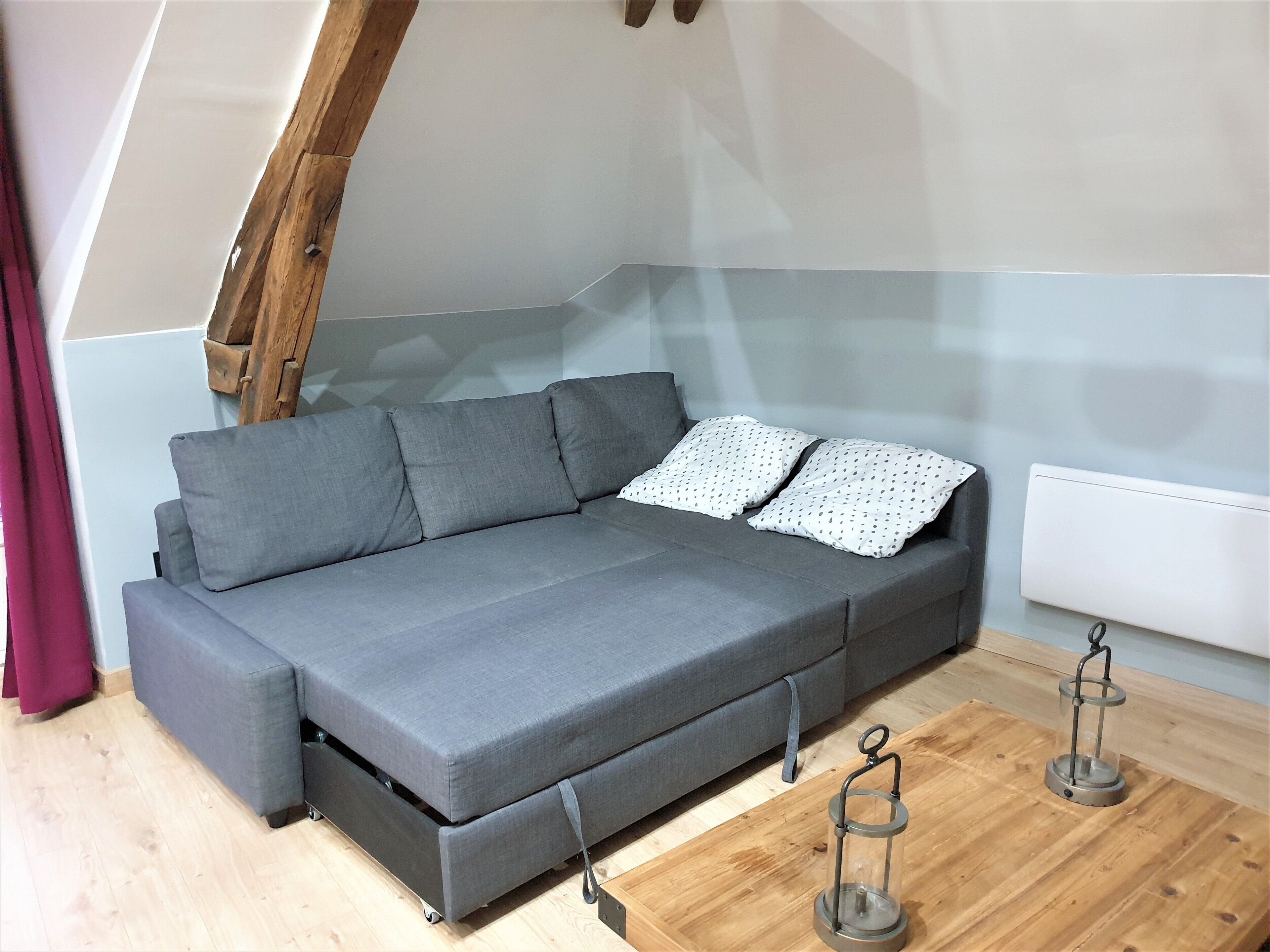 A grey sofa with a pull-out bed, a wooden ladder, and a small table with a lantern.