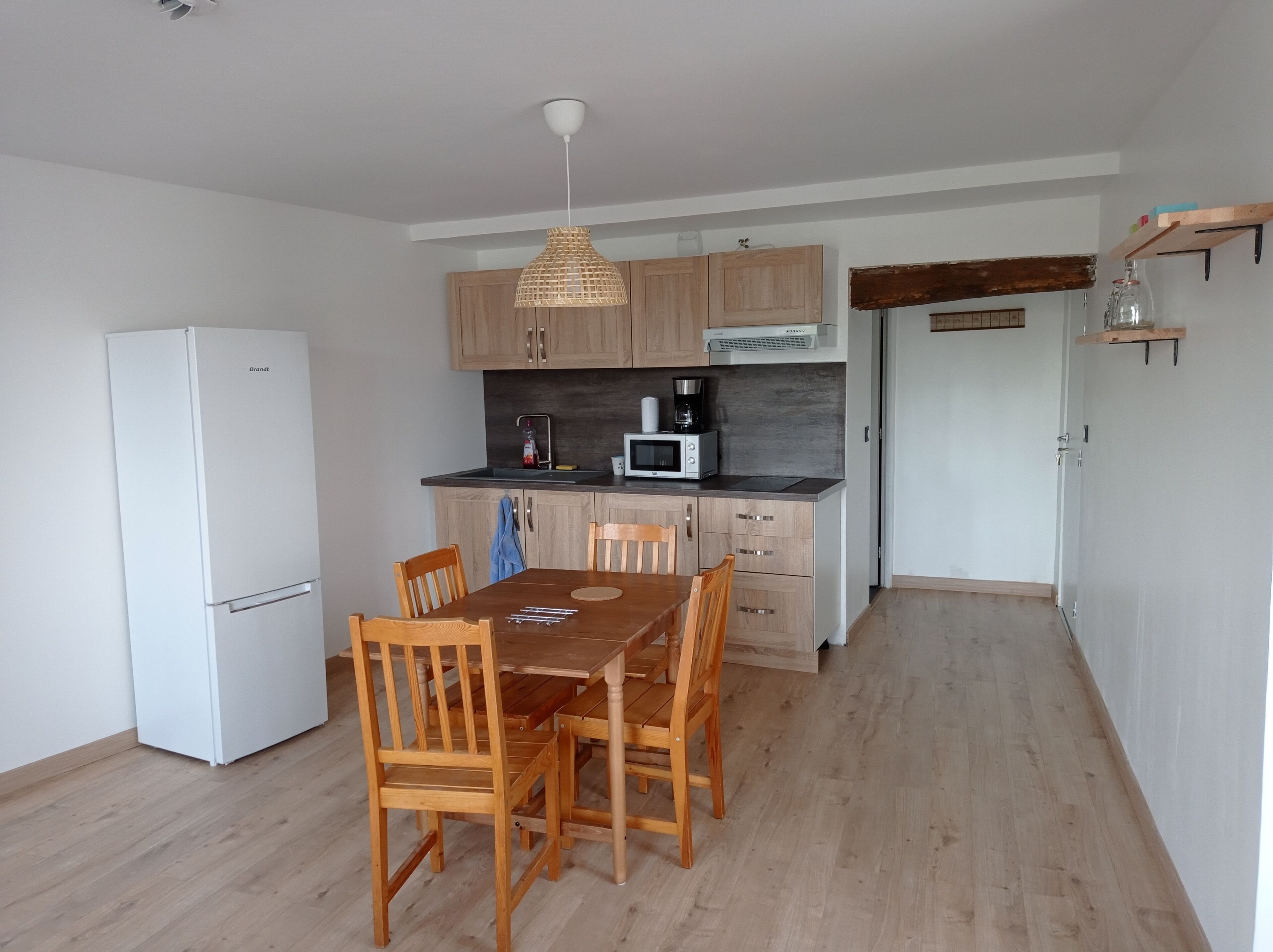 A compact kitchen with a white refrigerator, wooden cabinets, a microwave, and a hanging light fixture.
