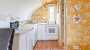 Een keuken met witte kastjes, een houten plafond en behang met gele bloemen.