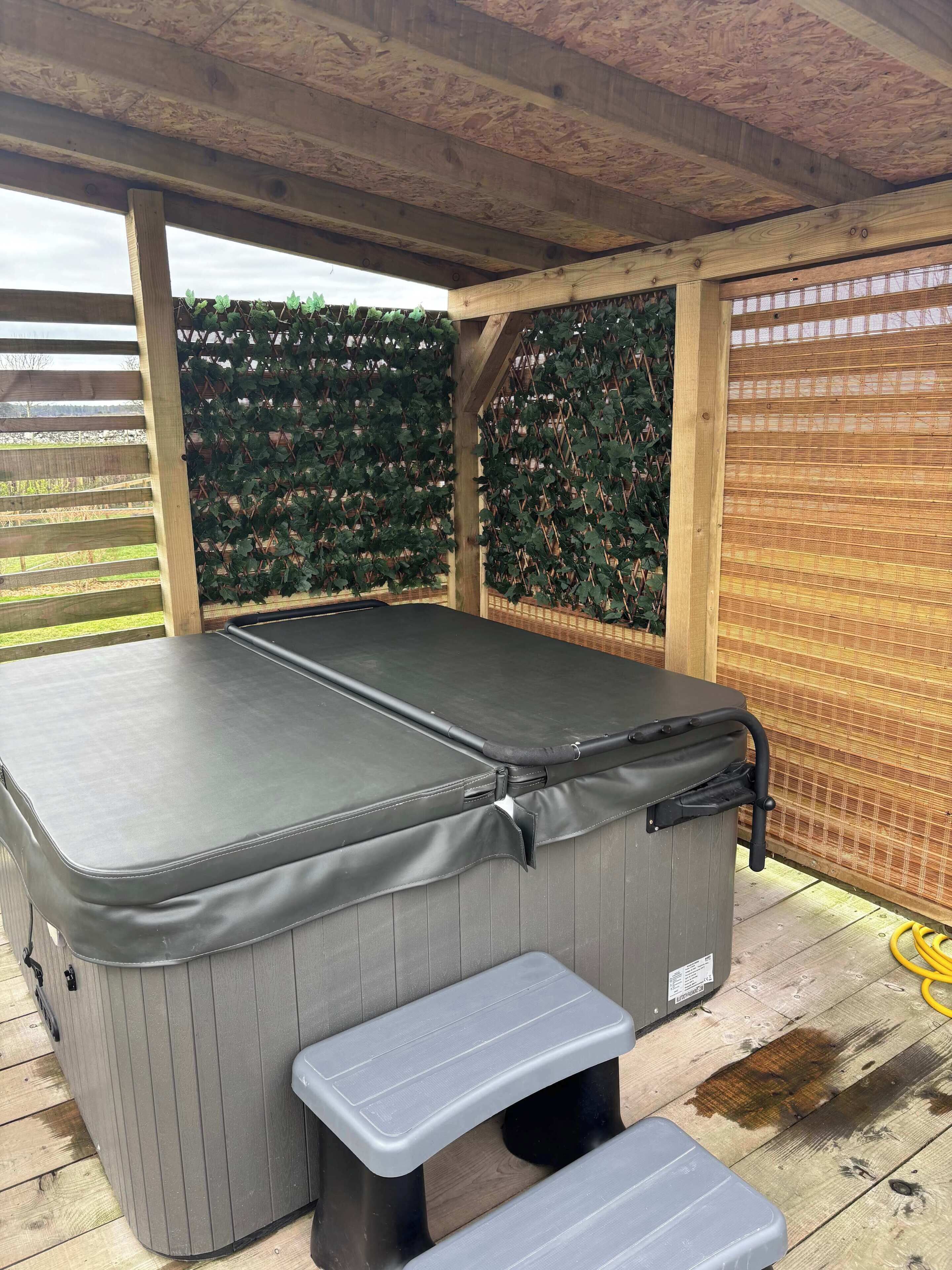 A hot tub with a bench, surrounded by wooden beams and a lattice fence with greenery.