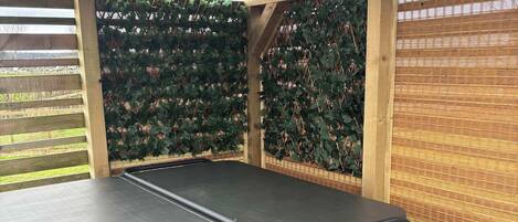 A hot tub with a bench, surrounded by wooden beams and a lattice fence with greenery.