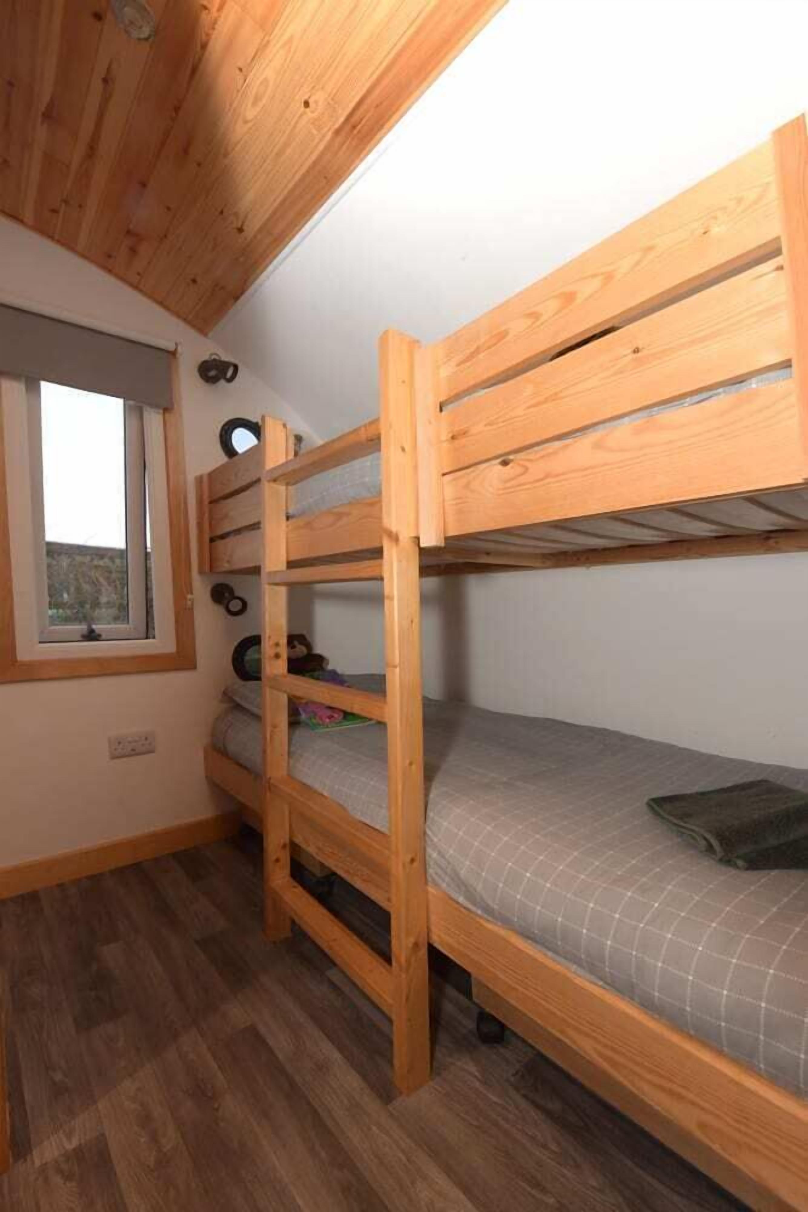 A bunk bed room with a window, wooden ceiling, and a small shelf with items.