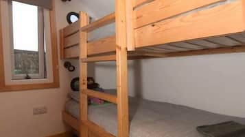 A bunk bed room with a window, wooden ceiling, and a small shelf with items.