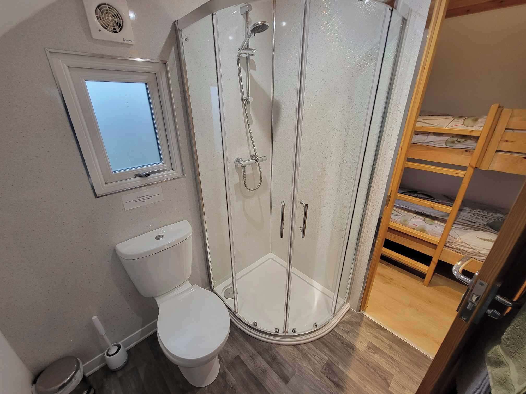 A bathroom with a toilet, a shower enclosure, a window, and a bunk bed.