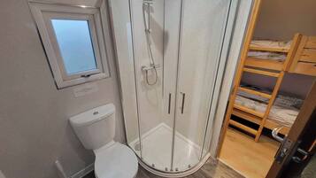 A bathroom with a toilet, a shower enclosure, a window, and a bunk bed.