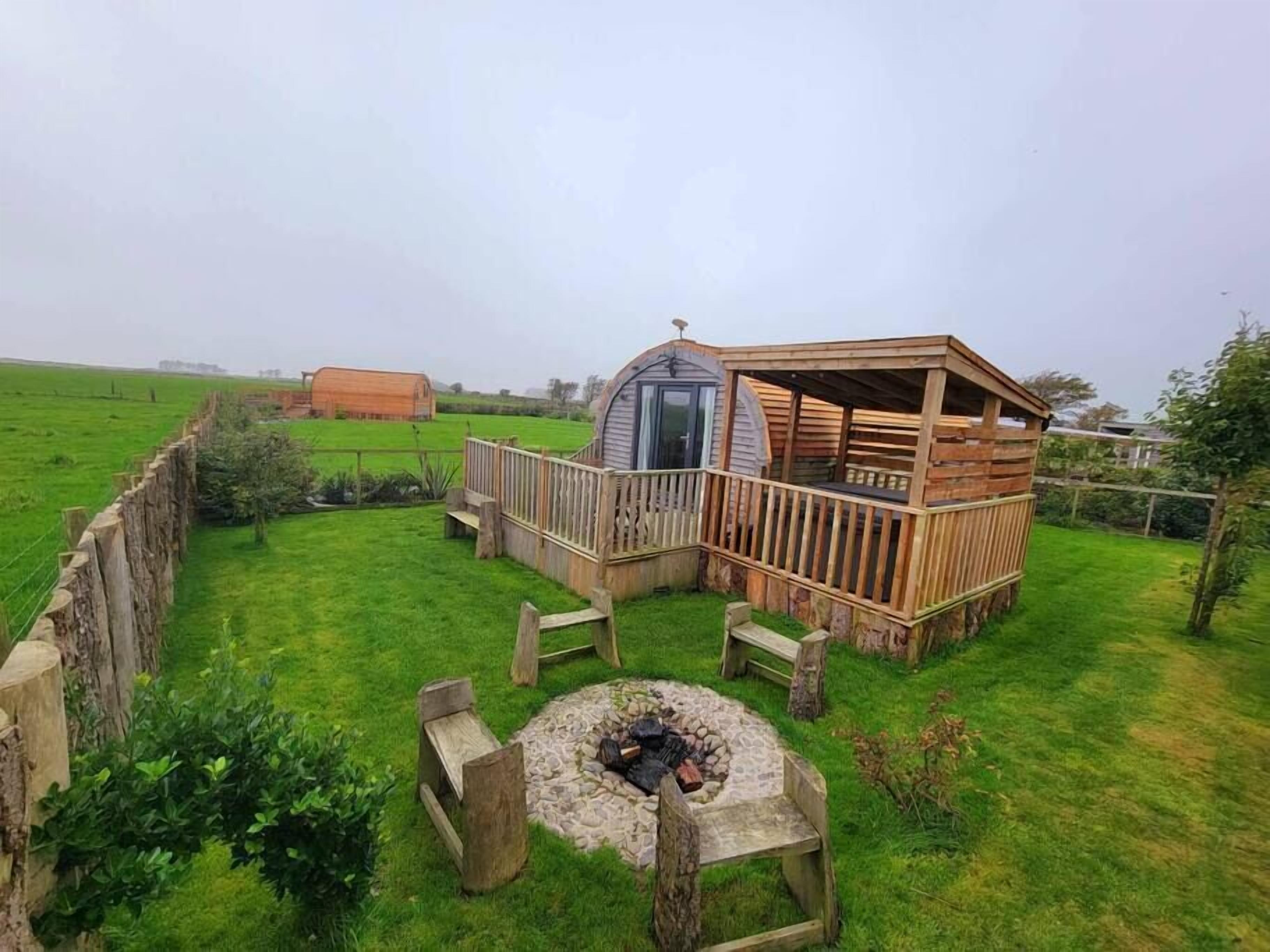 Een rustieke houten hut met terras, omringd door een omheind gazon en een vuurkorf van natuursteen.
