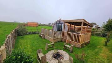 Een rustieke houten hut met terras, omringd door een omheind gazon en een vuurkorf van natuursteen.