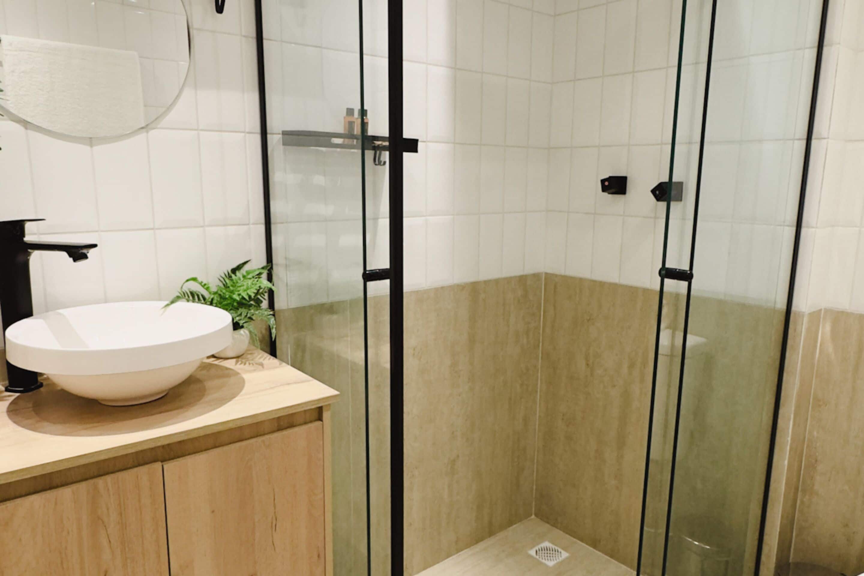 A modern bathroom with a round sink, a glass shower enclosure, and a potted plant.