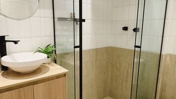 Un baño moderno con un lavabo redondo, cabina de ducha con mampara de cristal y una planta en maceta.