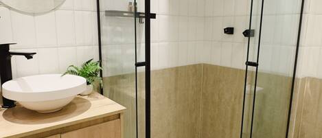 A modern bathroom with a round sink, a glass shower enclosure, and a potted plant.