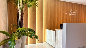 Un espace d’accueil avec un mur en bois, un comptoir de réception en marbre et de grandes plantes en pot.